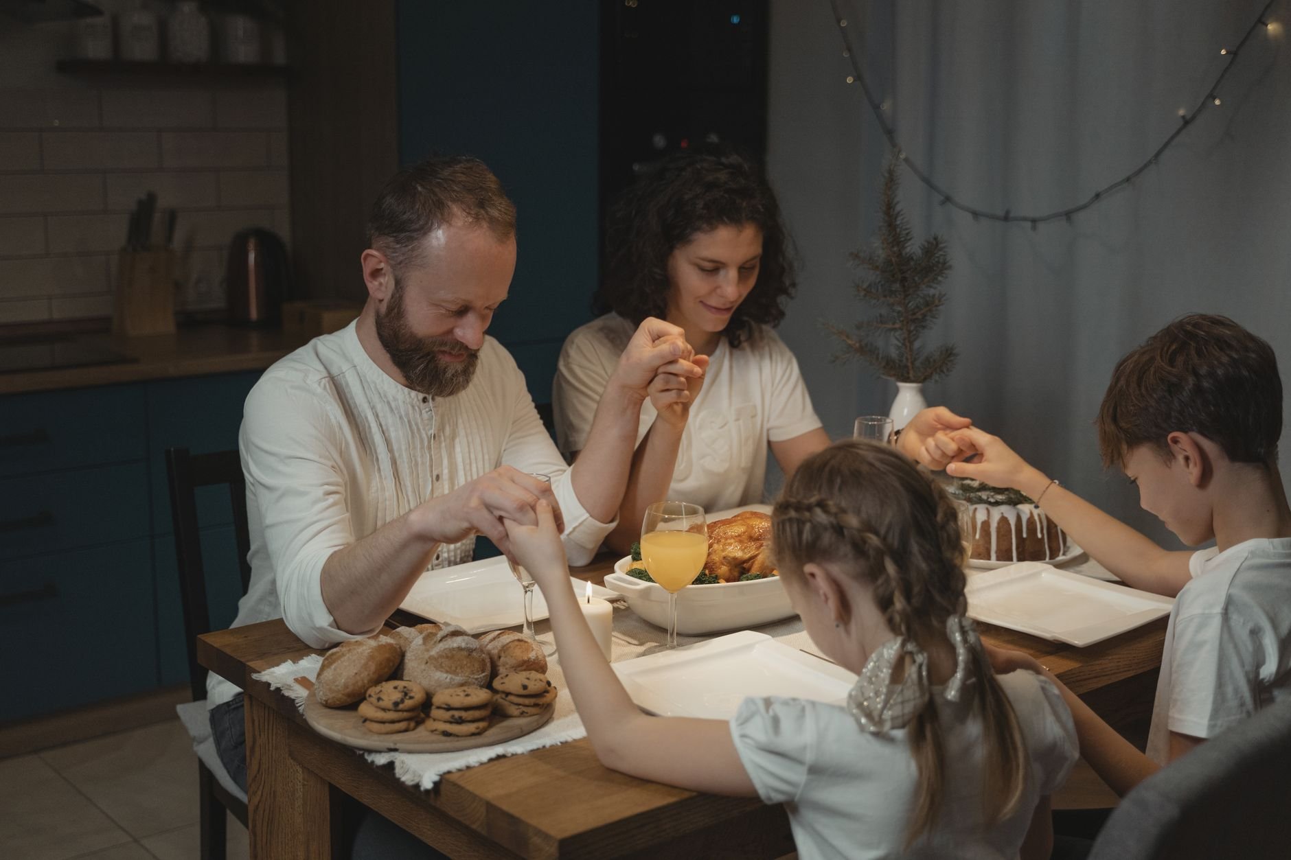Family holding hands and praying over a dinner table during a faith gathering.